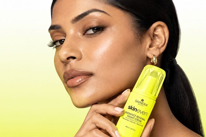 Woman with clear, even-looking skin holding a Skineven product